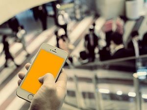 Hand holding a smartphone in a busy office, symbolizing business email compromise